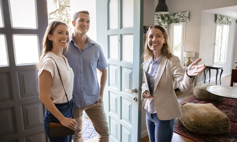 Couple standing in doorway of home as a women gestures for them to look inside