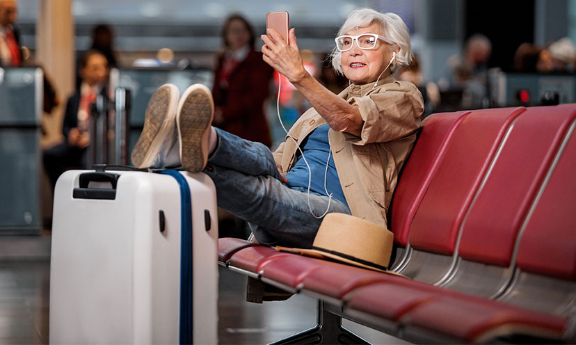 Woman holds up a phone while she sits in an airport terminal with her feet up on a suitcase